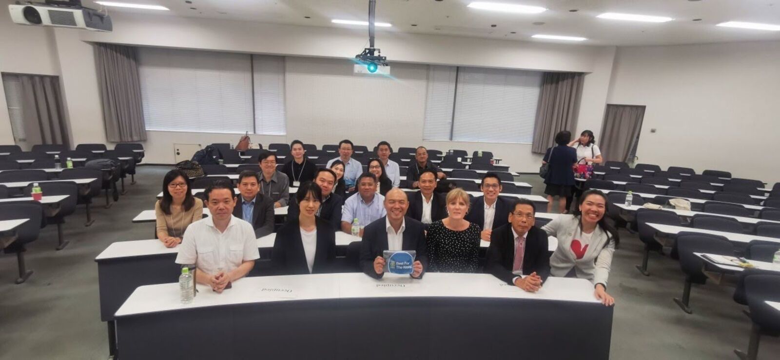 ภาพหมู่ในห้องบรรยายของมหาวิทยาลัยแห่งหนึ่งในญี่ปุ่น ผู้เข้าร่วมคนหนึ่งถือป้าย Best For The World