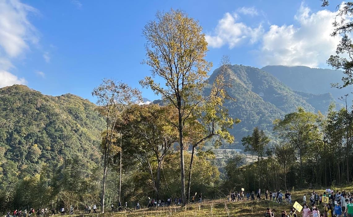 Green Tree Party: a long line of participants walking up a hillside toward the planting ground, mountains and blue sky behind