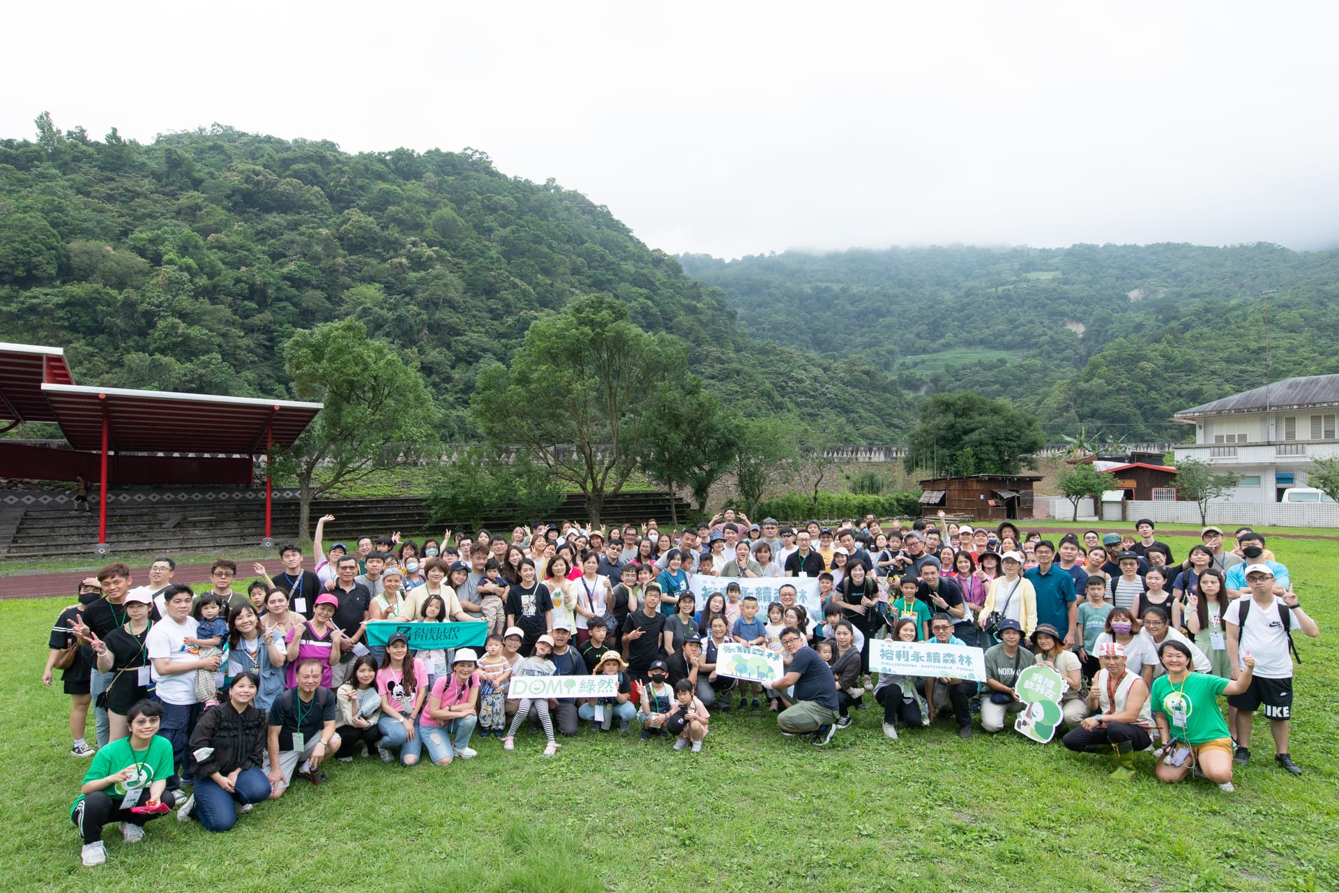 Group photo at the Zuellig sustainable-forest day — hundreds of employees and families on a village field with Zuellig Pharma and DOMI banners
