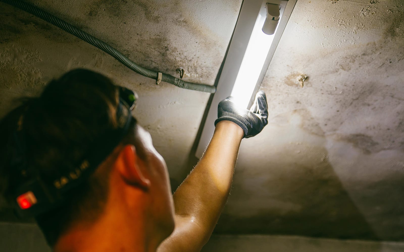 A volunteer in a headlamp replaces an energy-poor household's ceiling light with an energy-saving fixture