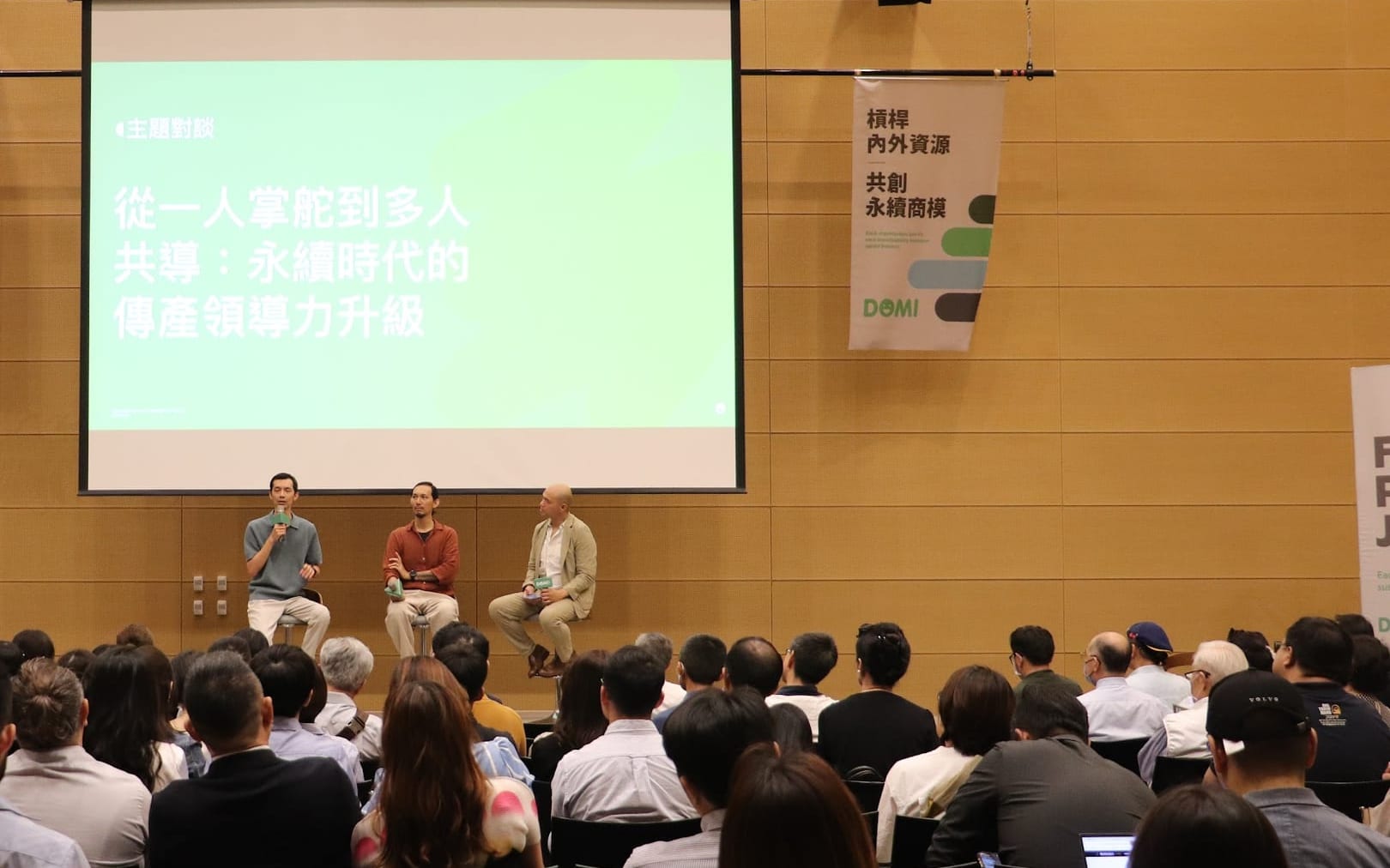 A sustainability business-model forum panel on stage in front of a full house