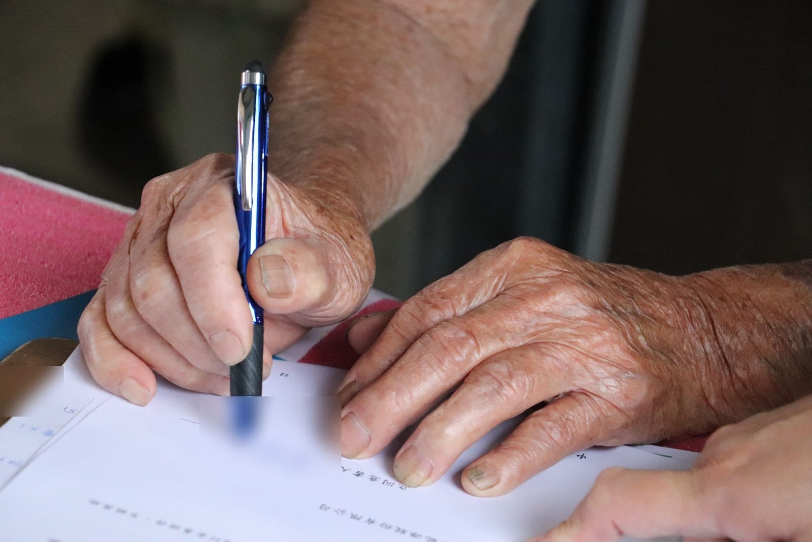 An elder's hands signing a participation form, a staff member's hand steadying the paper