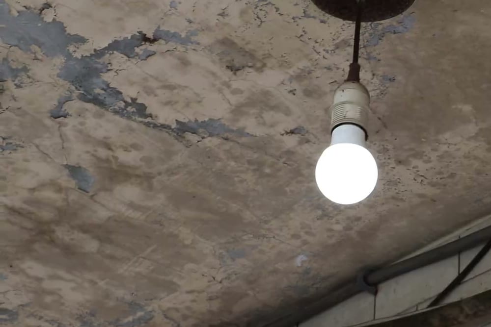 A new LED bulb glowing under the peeling ceiling of an old house